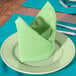 A folded seafoam green Intedge cloth napkin on a plate with silverware.