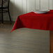 A square red Intedge tablecloth on a table with a plate.