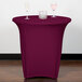 A table with a Snap Drape burgundy spandex round table cover and wine glasses on it.