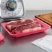 A CKF rose foam meat tray with raw meat on a counter.