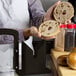 A person using a Baker's Mark black bagel slicer to slice two bagels.