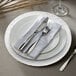 A white Charge It by Jay rattan charger plate with silverware and a napkin on it.