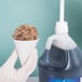 A gloved hand holding a white paper cone filled with a brown object next to a plastic jug.