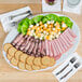 A Tuxton Alaska china platter with lettuce, cheese, and meat on it.