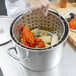 A person using a Vollrath Wear-Ever fryer pot to cook lobster and corn.