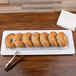 A white melamine display tray with a plate of bagels and tongs on a table.