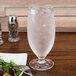 A close-up of a customizable Tritan plastic goblet filled with water on a table next to a salad plate.