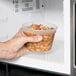A hand holding a Pactiv translucent round deli container of food.