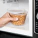 A hand holding a Pactiv translucent round deli container of food in a microwave.