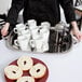 A person holding a Vollrath stainless steel oblong serving tray with white coffee cups and bagels.