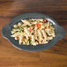 A Fiesta oval china baker filled with pasta and vegetables on a wood table.