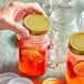 A person holding an Acopa Rustic Charm gold metal drinking jar with a red drink and a lemon slice.