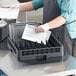 A man in a blue apron using a Noble Products full-size dish rack to put white plates in a dishwasher.