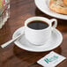 A Tuxton Colorado demitasse saucer with a cup of coffee and bread on a table.