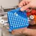 A hand using a blue Nemco push block cleaning gasket to cut a tomato.