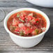 A Diamond White melamine bouillon filled with salsa on a wood table.