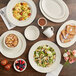 An Acopa ivory stoneware platter on a table with plates of food and drinks.