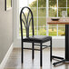 A black Lancaster Table & Seating chair with a black vinyl seat next to a dining table with a place setting.