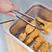 A person using tongs to serve fried chicken on a Footed Cooling Rack.