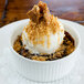 A white porcelain fluted ramekin filled with a dessert topped with ice cream and nuts.