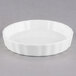 A white porcelain fluted creme brulee dish with a rim.