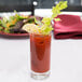 A close up of an Arcoroc Islande highball glass with a bloody mary and a lemon garnish on a table with a salad