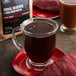 A glass cup of Crown Beverages Royal Reserve Guatemalan coffee on a red plate next to a bag of coffee beans.