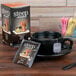 A black cup of Steep By Bigelow Organic Chai tea on a saucer with a package of black tea on the table.