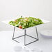 A white plate of salad on a black square display stand.