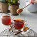 A honey dipper being used to pour Monarch's Choice honey into a glass of tea.