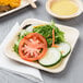 A EcoChoice palm leaf plate with salad, tomatoes, cucumbers, and lettuce on a table.