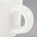 A close up of a Tuxton eggshell white china cup with a handle.