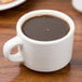 A Tuxton eggshell china cup filled with coffee on a table.