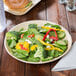 A TreeVive by EcoChoice palm leaf plate with a sandwich, broccoli, and spinach on it.
