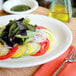 A Tuxton Nevada oval china platter with a salad of vegetables and herbs.