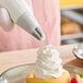 A person's hand using an Ateco closed star piping tip to pipe pastry cream onto a dessert.