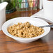 A bowl of cereal with a spoon in a white Arcoroc porcelain bowl.