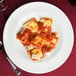 A Tuxton eggshell china pasta bowl filled with ravioli in sauce with a fork on the table.