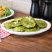A Tuxton Nevada narrow rim oval china platter with green ravioli on a table.