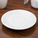 A Tuxton Reno white china saucer on a wood surface.