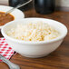 A bowl of rice with black seeds next to a Tuxton eggshell china bowl filled with soup.
