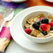 A Tuxton Reno ivory china plate with a bowl of cereal and berries on a table with a spoon.