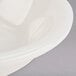 A close up of a Tuxton eggshell white china fruit bowl with a curved edge.
