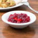 A Tuxton eggshell china bowl filled with cranberry sauce on a table with food and a fork.