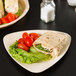 A TreeVive by EcoChoice triangular palm leaf plate with vegetables and corn on it.