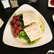 A TreeVive by EcoChoice palm leaf plate with a sandwich, grapes and a piece of fruit on a wooden surface.