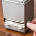 A hand pressing a button on a metal box.