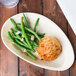 A TreeVive by EcoChoice oval palm leaf tray with green beans and a biscuit on a wooden table.