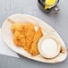 An EcoChoice palm leaf tray with fried chicken and sauce on a table.