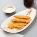 An oval palm leaf tray with fried chicken on a table.